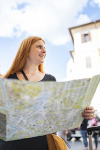 Pretty red hair woman with a city map is smiling looking around