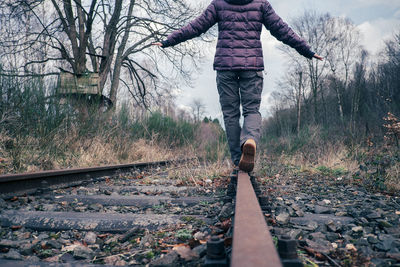 Rear view of person balancing while walking on railroad track