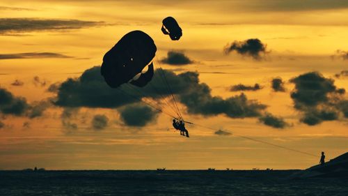 People paragliding over sea against sky during sunset