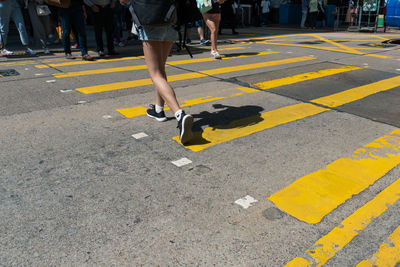 Low section of people crossing road in city during sunny day