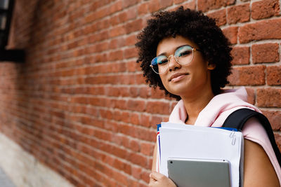 Portrait of young woman looking away against brick wall