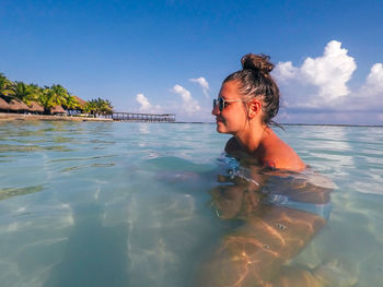Side view of smiling young woman swimming in sea against blue sky