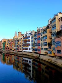 Buildings by river against clear blue sky