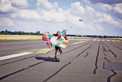 Rear view of person holding colorful shawl while skating on airport runway