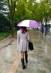 Full length rear view of woman with umbrella walking on footpath in city during monsoon