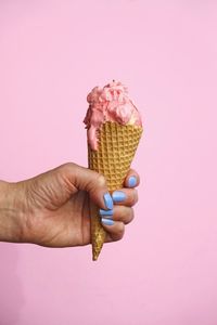 Hand with blue fingernails holding ice cream cone against pink background