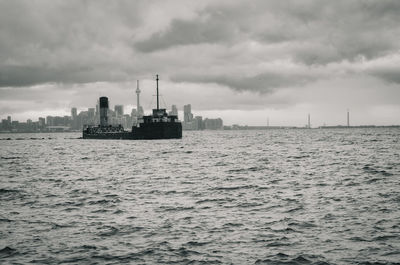 Ship sailing in sea against cloudy sky