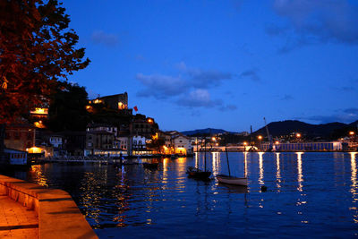 Sailboats moored on illuminated canal by buildings in city at night