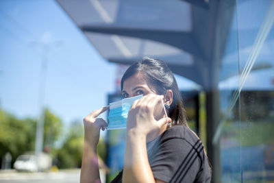 Woman at bus stop putting mask on her face