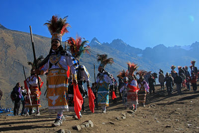 People in traditional clothing dancing on sand against mountains and sky