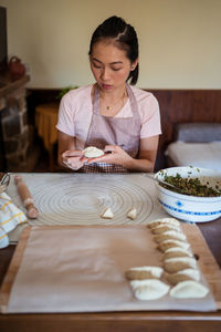 Woman in casual clothes and apron stuffing dumplings with meat while preparing traditional chinese jiaozi in kitchen