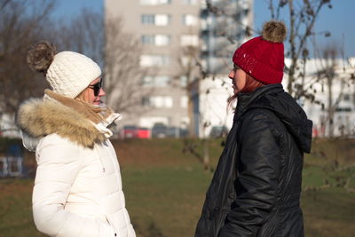 Side view of women wearing warm clothing while standing on grass during winter