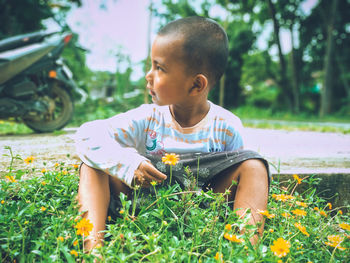 Cute boy looking away while sitting on plants