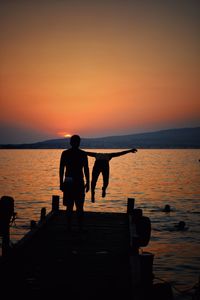 Rear view of man on pier looking at friend jumping into sea during sunset