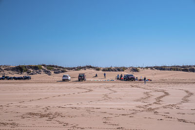 Tourists with quadbikes, cars and surfboards on sand