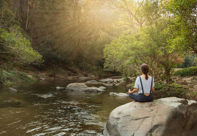 Boy sitting on rock by river in forest