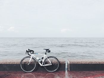 Bicycles parked by sea against sky