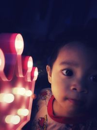 Close-up of cute boy by illuminated light at night