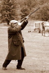 Side view of senior man aiming gun while standing on grassy field