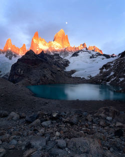 Scenic view of lake by snowcapped mountains against sky during sunset