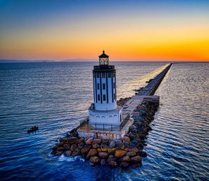 Lighthouse by sea against sky during sunset