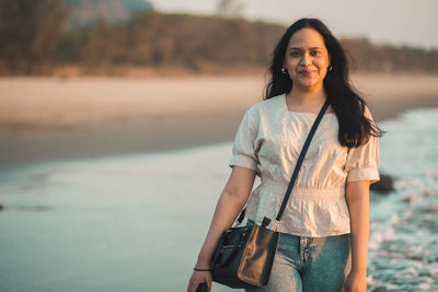 Young woman standing on the beach against sea during sunset