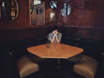 Depressed young woman with hands on chin sitting in restaurant
