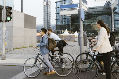 Male and female business colleagues with bicycles waiting at stoplight while commuting to office in city