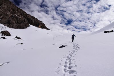 Hiker climbing on snow covered mountains against cloudy sky
