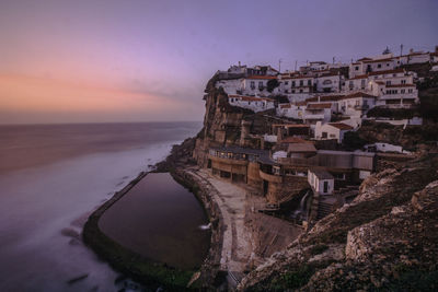 Buildings by sea against sky at sunset