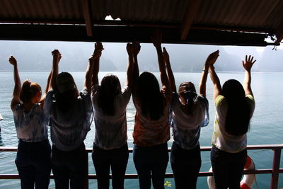 Female friends with arms raised standing against sea