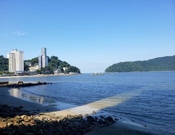 Scenic view of sea by buildings against clear blue sky