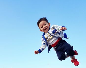 Low angle view of smiling boy against clear blue sky