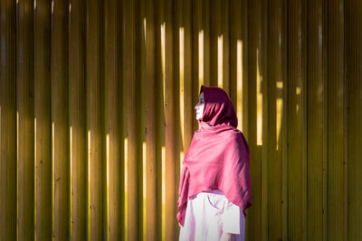 Woman wearing headscarf while standing against yellow corrugated iron