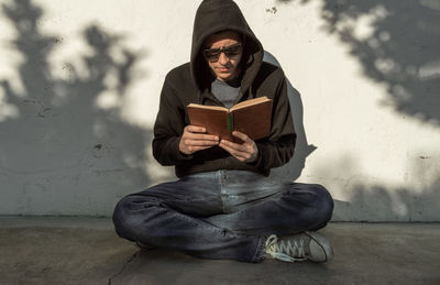 Young man sitting on book against wall