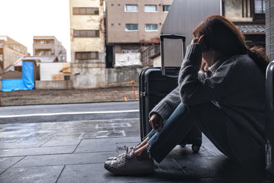 Side view of woman sitting on sidewalk in city