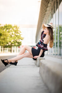 Side view of smiling young woman sitting on footpath