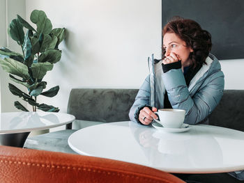 Woman looking away while sitting with coffee cup at table