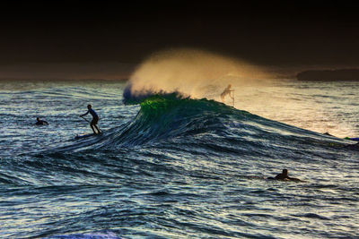 People swimming in sea against sky during sunset