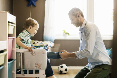 Smiling father dressing up son at home on sunny day