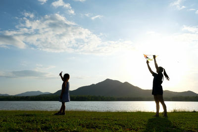 Rear view of woman with arms outstretched standing at beach against sky