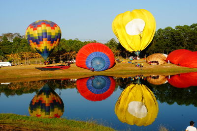 Multi colored hot air balloon flying over lake against sky