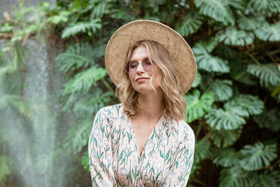 Beautiful young woman in a straw hat and glasses in the park on a background of greenery