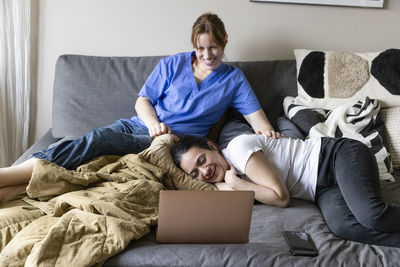 Female caregiver and woman with disability watching movie on laptop sitting at home