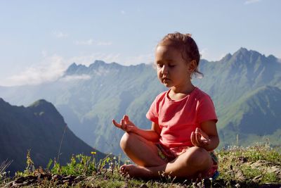 Girl meditating while sitting on mountain against sky