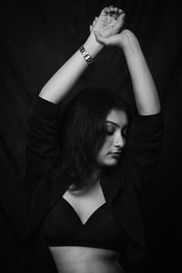 Portrait of young woman standing against black background