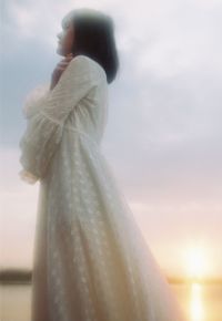 Side view of woman standing against sky during sunset