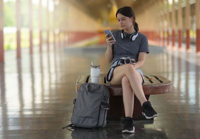 Female traveler looking at smartphone while waiting for train on platform..