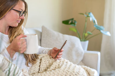 Midsection of woman holding mobile phone at home