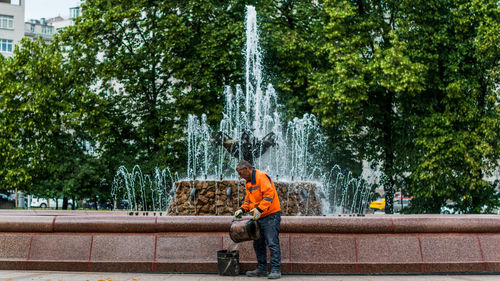 Side view of male worker pouring water in bucket by fountain